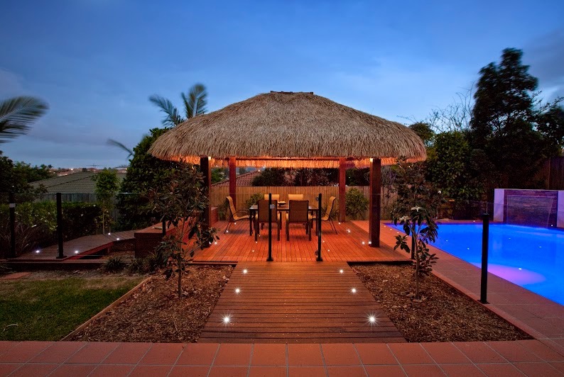 Luxury Balinese hut with thatched roof, timber deck, and pool lighting at dusk.
